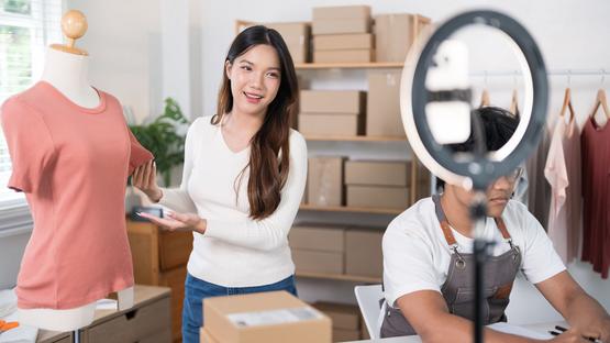 Live Shopping: Frau nimmt T-Shirt mit Stativ und Handy auf
